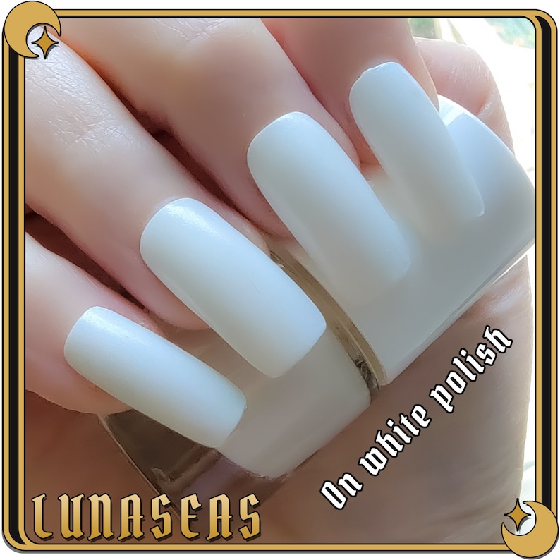 Puede incluir: U&ntilde;as largas de forma cuadrada pintadas con un esmalte de u&ntilde;as blanco s&oacute;lido y opaco. El texto "LUNASEAS" aparece en la esquina inferior izquierda y el texto "On white polish" est&aacute; impreso en la zona inferior derecha.