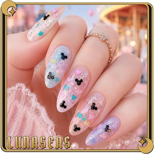 K&ouml;nnte beinhalten: Mandelformige Fingern&auml;gel mit transparenter Basis, irisierendem Glitzer, kleinen schwarzen Mausohr-Silhouetten und winzigen pastellfarbenen Herzen in Rosa, Blau und Gelb. Ein d&uuml;nner goldener Ring mit einem kleinen Mausohr-Anh&auml;nger am Ringfinger.