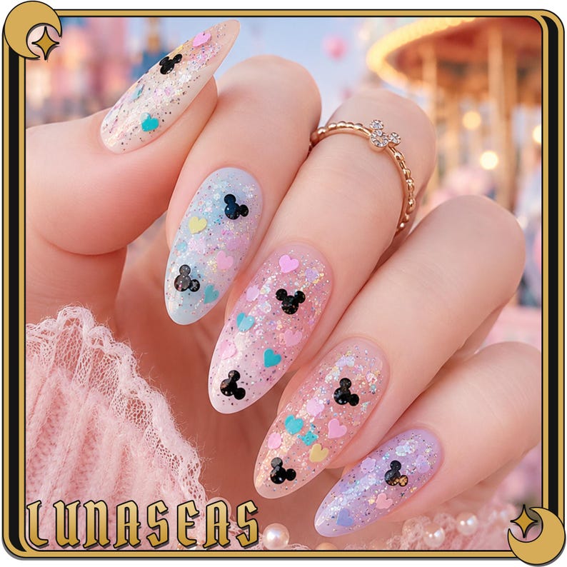 K&ouml;nnte beinhalten: Mandelformige Fingern&auml;gel mit transparenter Basis, irisierendem Glitzer, kleinen schwarzen Mausohr-Silhouetten und winzigen pastellfarbenen Herzen in Rosa, Blau und Gelb. Ein d&uuml;nner goldener Ring mit einem kleinen Mausohr-Anh&auml;nger am Ringfinger.