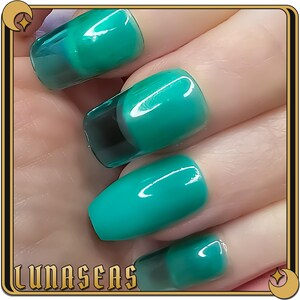 May include: Close-up of a hand with four teal green nail tips. The nail tips have a clear, glossy finish and a black accent at the base.