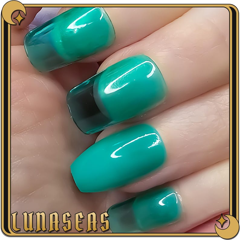 May include: Close-up of a hand with four teal green nail tips. The nail tips have a clear, glossy finish and a black accent at the base.