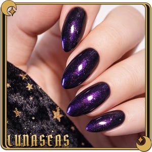 May include: Close-up of a hand with four long, oval-shaped nails painted a deep purple with a shimmering, glittery effect. The nails have a glossy finish. The word "LUNASEAS" is at the bottom of the image.