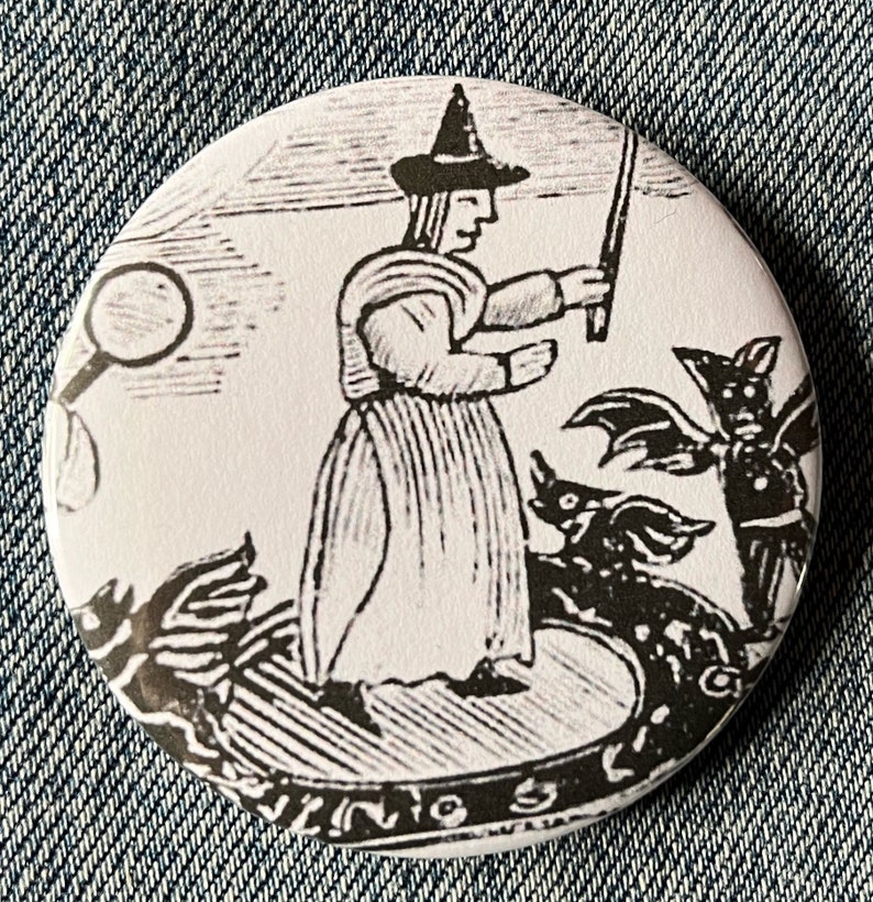 May include: Black and white illustration of a witch with a pointed hat and a wand, surrounded by bats and other creatures. The image is printed on a round button.