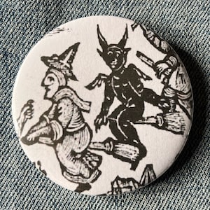 May include: A white button with a black and white illustration of three figures flying on broomsticks. The figures are a witch, a devil, and another witch. The illustration is in a vintage style.