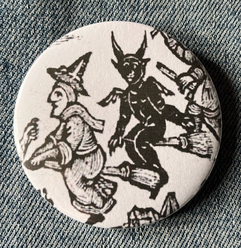 May include: A white button with a black and white illustration of three figures flying on broomsticks. The figures are a witch, a devil, and another witch. The illustration is in a vintage style.