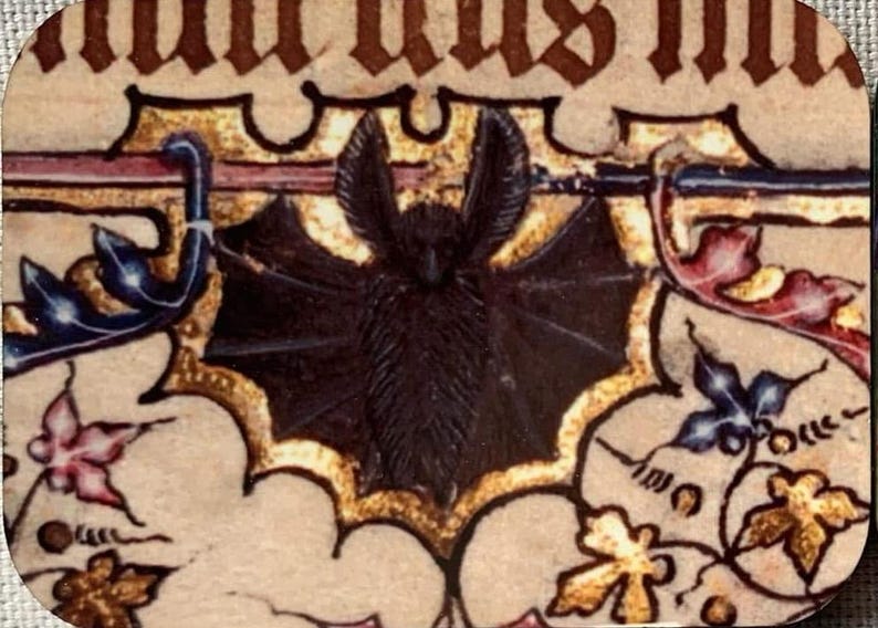 K&ouml;nnte beinhalten: Eine schwarze Fledermaus mit ausgebreiteten Fl&uuml;geln ist in einem mittelalterlichen illuminierten Manuskript dargestellt. Die Fledermaus ist von goldenen und roten floralen Designs umgeben.