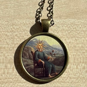 May include: A gold chain necklace with a round pendant featuring a painting of a person with a sun for a head sitting on a throne. The person is wearing a blue robe and holding a flower.
