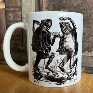 May include: White ceramic mug with a black and white illustration of two frogs dancing. The mug has a black handle and the text "J.S.S" and "Jarrqult" on the bottom.