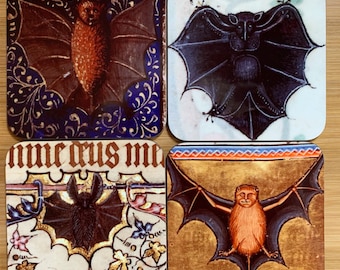 May include: Set of four coasters featuring vintage illustrations of bats. Each coaster has a different bat design with intricate details and a gold background. The coasters are made of cork and are perfect for protecting your furniture from scratches and spills.