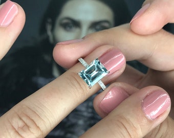 May include: A silver ring with a large, rectangular, light blue gemstone surrounded by smaller, clear gemstones.