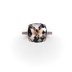 May include: A rose gold ring with a large, square-shaped, brown gemstone surrounded by smaller, clear gemstones.