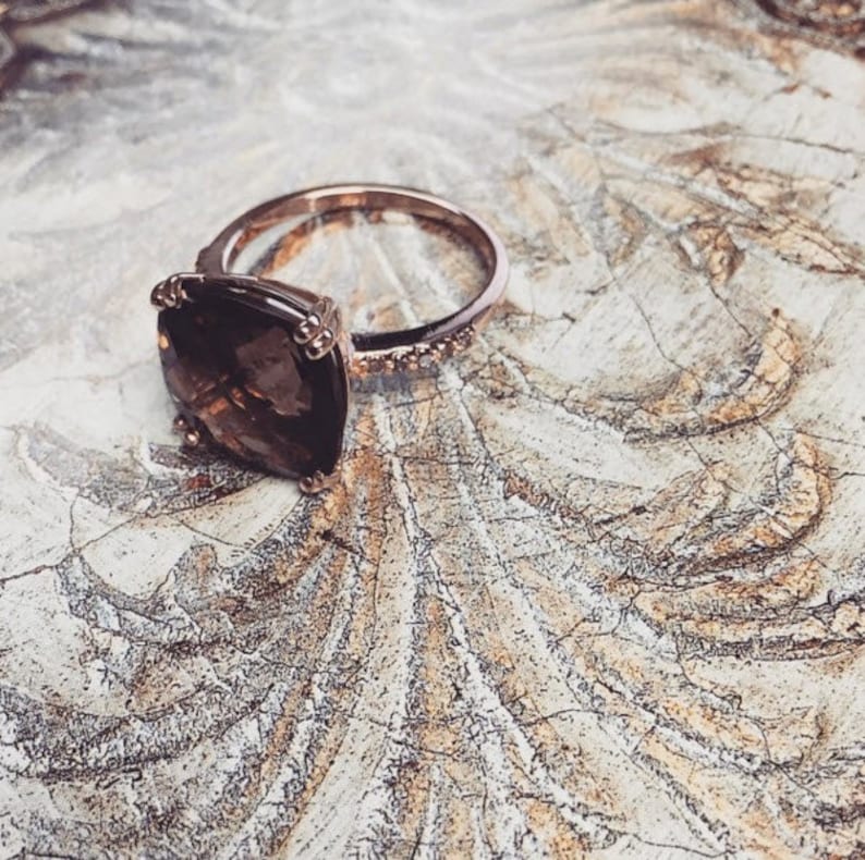 May include: A rose gold ring with a large, square-shaped, brown gemstone. The ring has a band of small diamonds.
