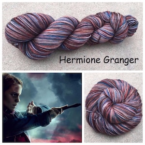 May include: A skein of hand-dyed yarn featuring a variegated color palette of deep red, navy blue, and soft grey tones. The text Hermione Granger is printed below the yarn. A smaller image shows a character holding a wand against a stormy sky.
