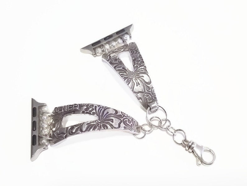 May include: Silver watch band with a floral design and clear rhinestones. The band has a clasp that can be attached to a watch.