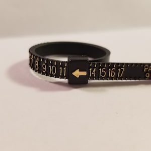 May include: Black plastic ring sizer with gold numbers 7 through 17 and an arrow pointing to the left. The text "PAT. PEND. 9101593" is printed on the ring sizer.