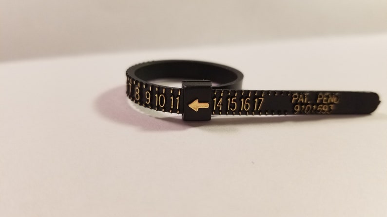 May include: Black plastic ring sizer with gold numbers 7 through 17 and an arrow pointing to the left. The text "PAT. PEND. 9101593" is printed on the ring sizer.
