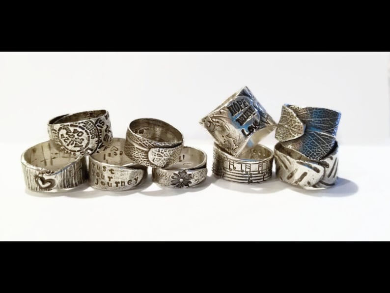 May include: A collection of eight silver rings with various designs and engravings. Some rings feature words like "Hope", "Love", and "Trust Your Journey".
