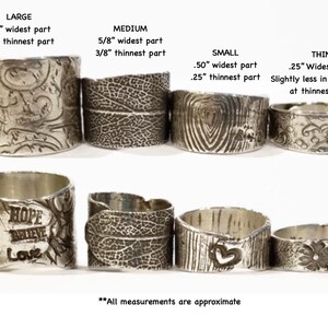May include: A set of eight silver rings with different designs and widths. The rings are arranged in two rows, with the largest ring on the left and the smallest ring on the right. The rings are all made of silver and have a textured surface. The rings are all approximately 3/8 inch thick.
