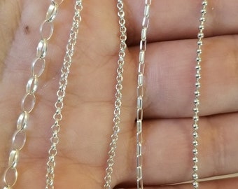 Puede incluir: Cuatro cadenas de plata de diferentes estilos, incluyendo una cadena de cable, una cadena de caja, una cadena de borde y una cadena de bola, se muestran en una mano.