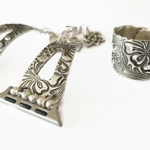 May include: Silver watch band with a floral design and a matching silver ring with a floral design.