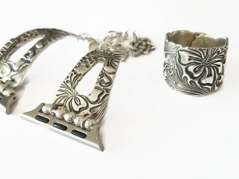 May include: Silver watch band with a floral design and a matching silver ring with a floral design.