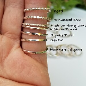 Pu&ograve; includere: Una collezione di anelli d'argento in vari design, tra cui modelli con perline, martellati e quadrati. Gli anelli sono esposti su un dito, mostrando le loro diverse trame e forme. Il testo sull'immagine recita "Bead", "Hammered Bead", "Medium Honeycomb", "Medium Round", "Square Twist", "Square", e "Hammered Square".