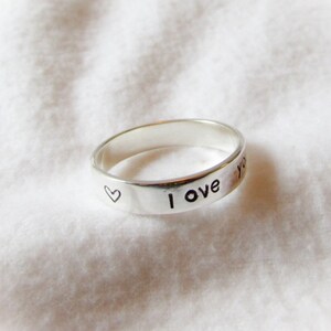 May include: A silver ring with the words "I love you" and a small heart engraved on the band.