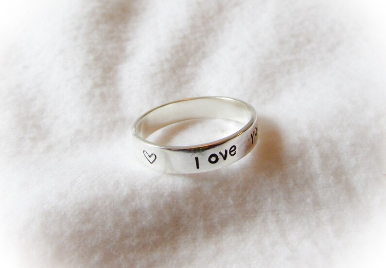 May include: A silver ring with the words "I love you" and a small heart engraved on the band.