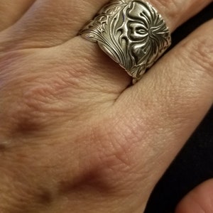 May include: A silver ring with a floral design. The ring is wide and has a detailed pattern.