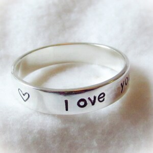 May include: A silver ring with the words "I love you" and a heart engraved on the band.