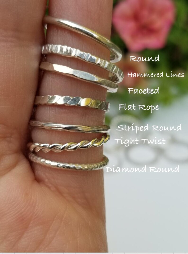 Pu&ograve; includere: Una mano mostra una collezione di anelli d'argento con vari design. Gli anelli includono una fascia rotonda liscia, una fascia con linee martellate, una fascia sfaccettata, una fascia piatta a corda, una fascia rotonda a righe, una fascia a torsione stretta e una fascia rotonda a diamante.