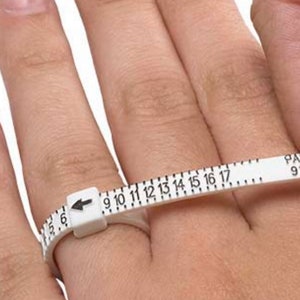 May include: White plastic ring sizer with black numbers from 6 to 17. The sizer is wrapped around a finger to determine ring size.