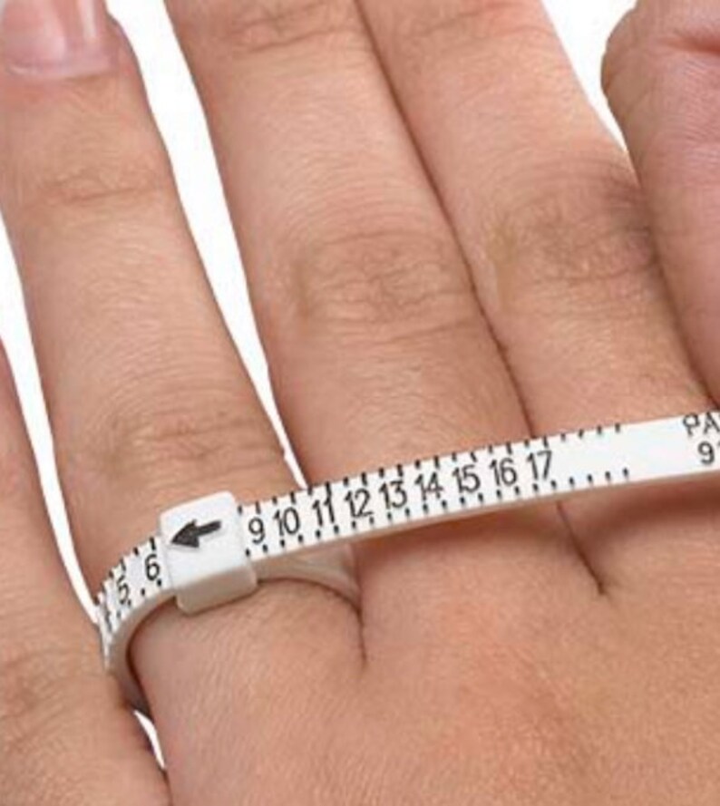 May include: White plastic ring sizer with black numbers from 6 to 17. The sizer is wrapped around a finger to determine ring size.
