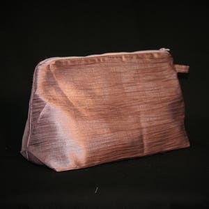 Puede incluir: Una bolsa de maquillaje de satén marrón claro con cierre de cremallera.