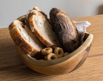 Könnte beinhalten: Eine Holzschale gefüllt mit Brotscheiben und kleinen, ringförmigen Snacks. Die Schale ist aus hellbraunem Holz mit dunkelbraunen Streifen.