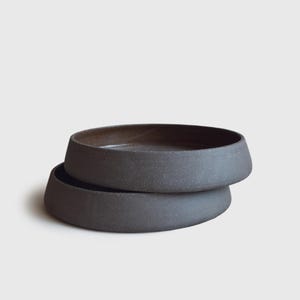 May include: Two black ceramic bowls stacked on top of each other. The bowls have a rough, textured surface and a slightly rounded shape.