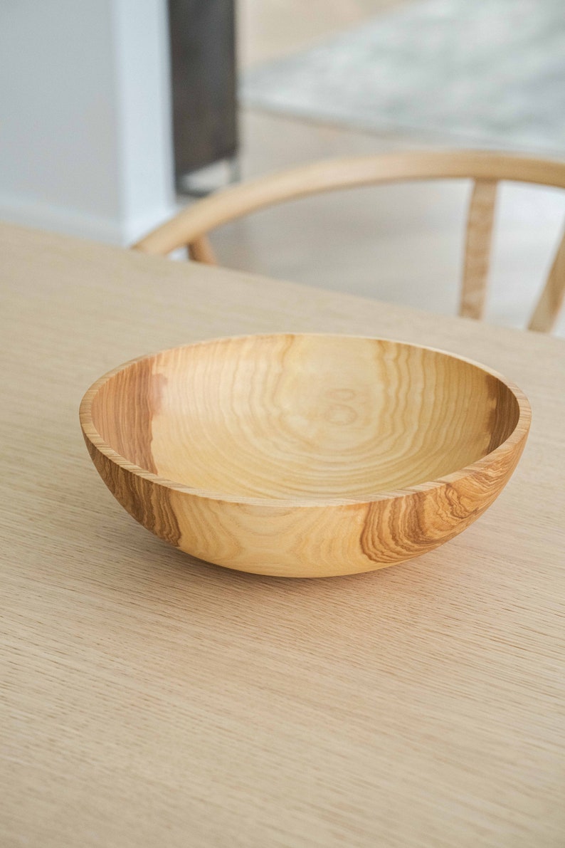 May include: A large, light brown wooden bowl with a smooth, rounded interior. The bowl is made of natural wood with visible grain patterns.