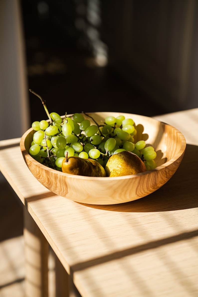 May include: A wooden bowl filled with green grapes and two pears. The bowl is on a light wood table.