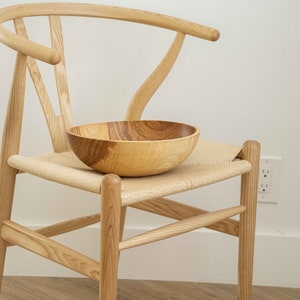 May include: A wooden bowl sits on a woven chair seat. The chair is made of light wood and has a curved back.