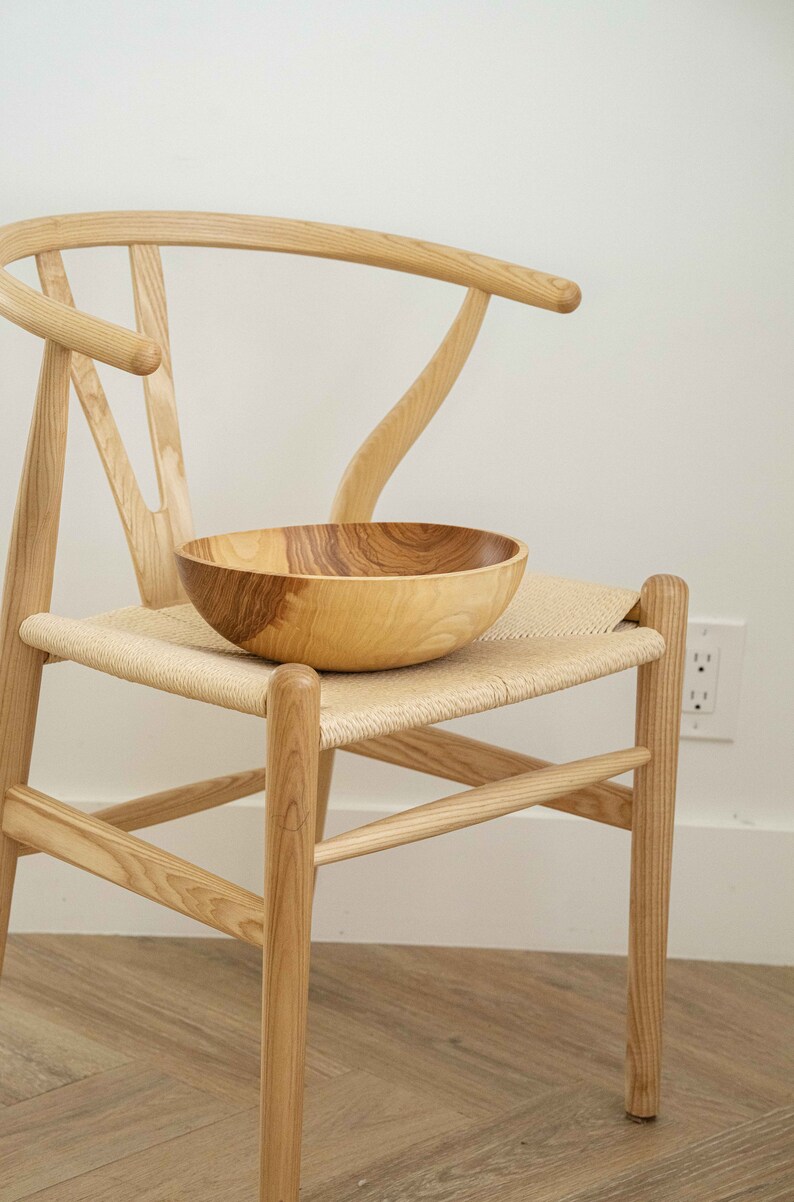 May include: A wooden bowl sits on a woven chair seat. The chair is made of light wood and has a curved back.