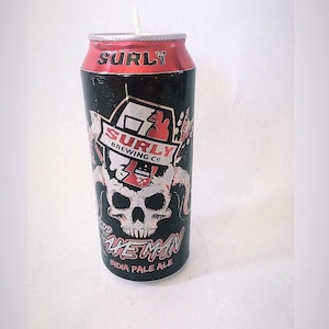 May include: A candle in the shape of a beer can. The can is black with a red top and features the text "SURLY" and "AXE MAN INDIA PALE ALE". A skull graphic is also visible.