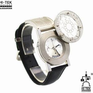 May include: A silver wristwatch with a black leather band. The watch face has a unique design with three small figures and a rotating dial. The watch has a circular, rotating bezel with the text "HI-TEK DESIGNS LONDON ALEXANDER" printed on it.