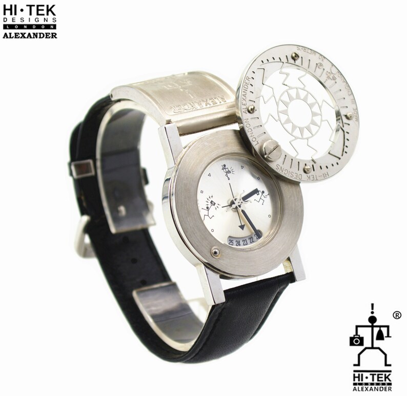 May include: A silver wristwatch with a black leather band. The watch face has a unique design with three small figures and a rotating dial. The watch has a circular, rotating bezel with the text "HI-TEK DESIGNS LONDON ALEXANDER" printed on it.