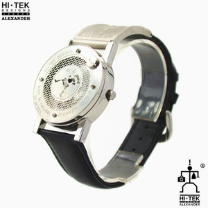 May include: A silver wristwatch with a black leather strap. The watch face is a skeleton design with a visible movement. The back of the watch has the text "HI-TEK DESIGNS", "30 METRES", "MADE IN ENGLAND", and "ALEXANDER".