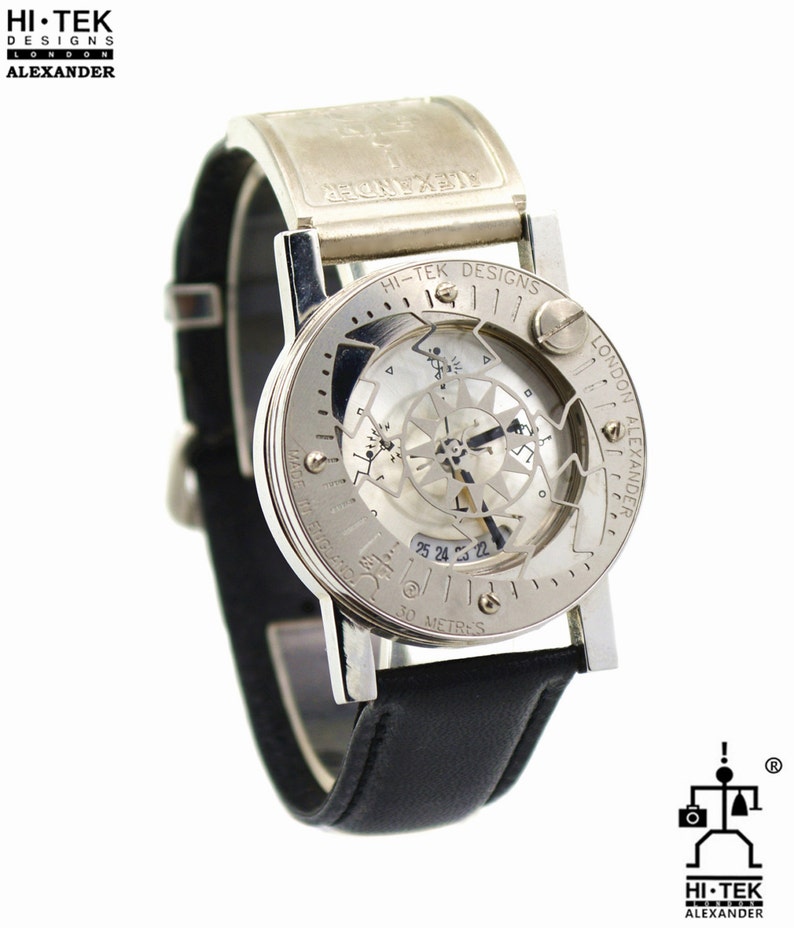 May include: A silver and black wristwatch with a skeletonized dial and a compass feature. The watch face has the text "HI-TEK DESIGNS LONDON ALEXANDER" and "MADE IN ENGLAND". The watch is water resistant to 30 meters.