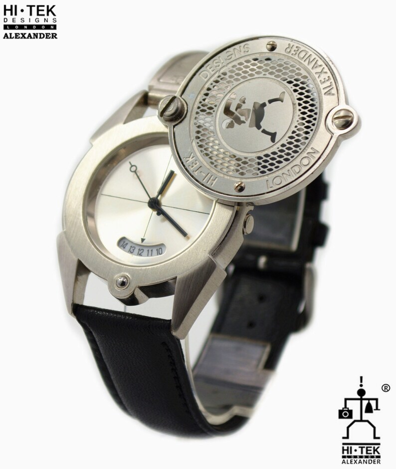 May include: A silver wristwatch with a black leather band. The watch face is white with black hands and numbers. The watch has a unique design with a circular cover that can be flipped open to reveal a silver design with the text "HI-TEK DESIGNS LONDON ALEXANDER".