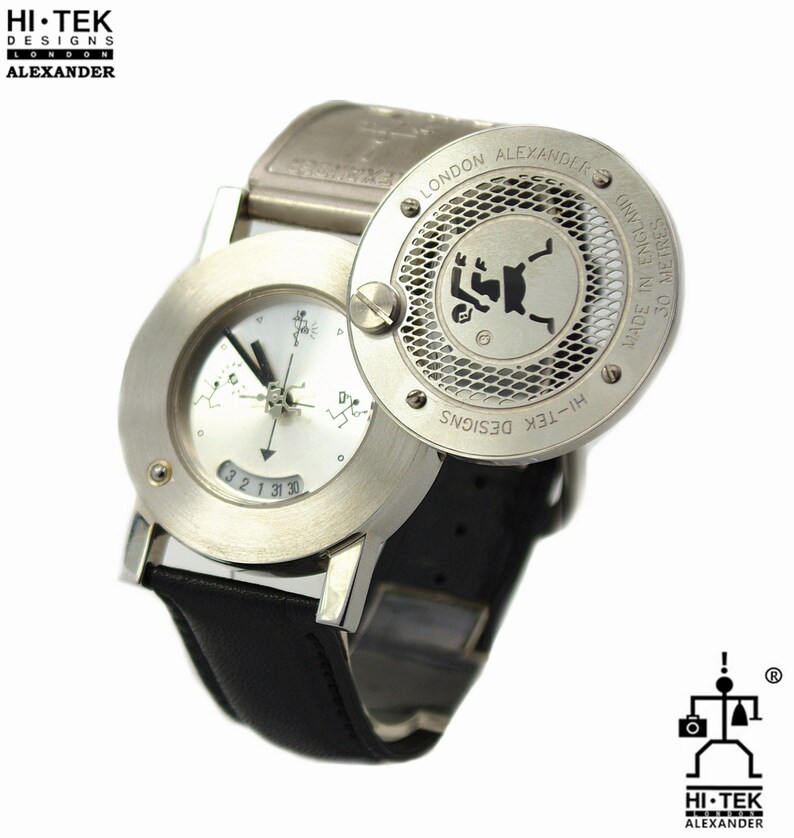 May include: A silver wristwatch with a black leather band. The watch face has a white background with black markings and a small compass. The watch has a round, silver case with a grid pattern and the text "HI-TEK DESIGNS LONDON ALEXANDER" on the back.