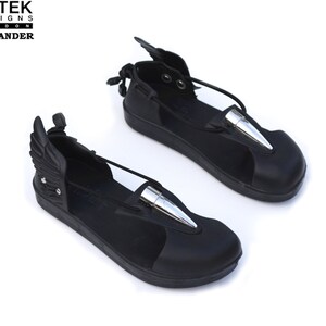 May include: Black leather sandals with silver bullet accents and attached wings. The sandals have a strap across the foot and an ankle strap.