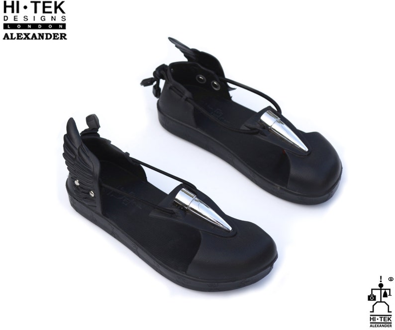 May include: Black leather sandals with silver bullet accents and attached wings. The sandals have a strap across the foot and an ankle strap.