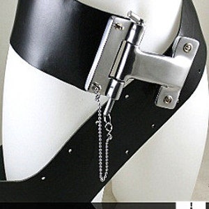 May include: A black leather belt with a silver metal buckle and a chain attached. The buckle is shaped like a hinge and has a small metal loop on the side. The belt is worn on a mannequin.
